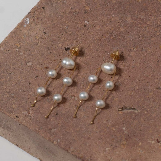 Brinco ouro 18k 5 perolas apoiado em fundo de pedra