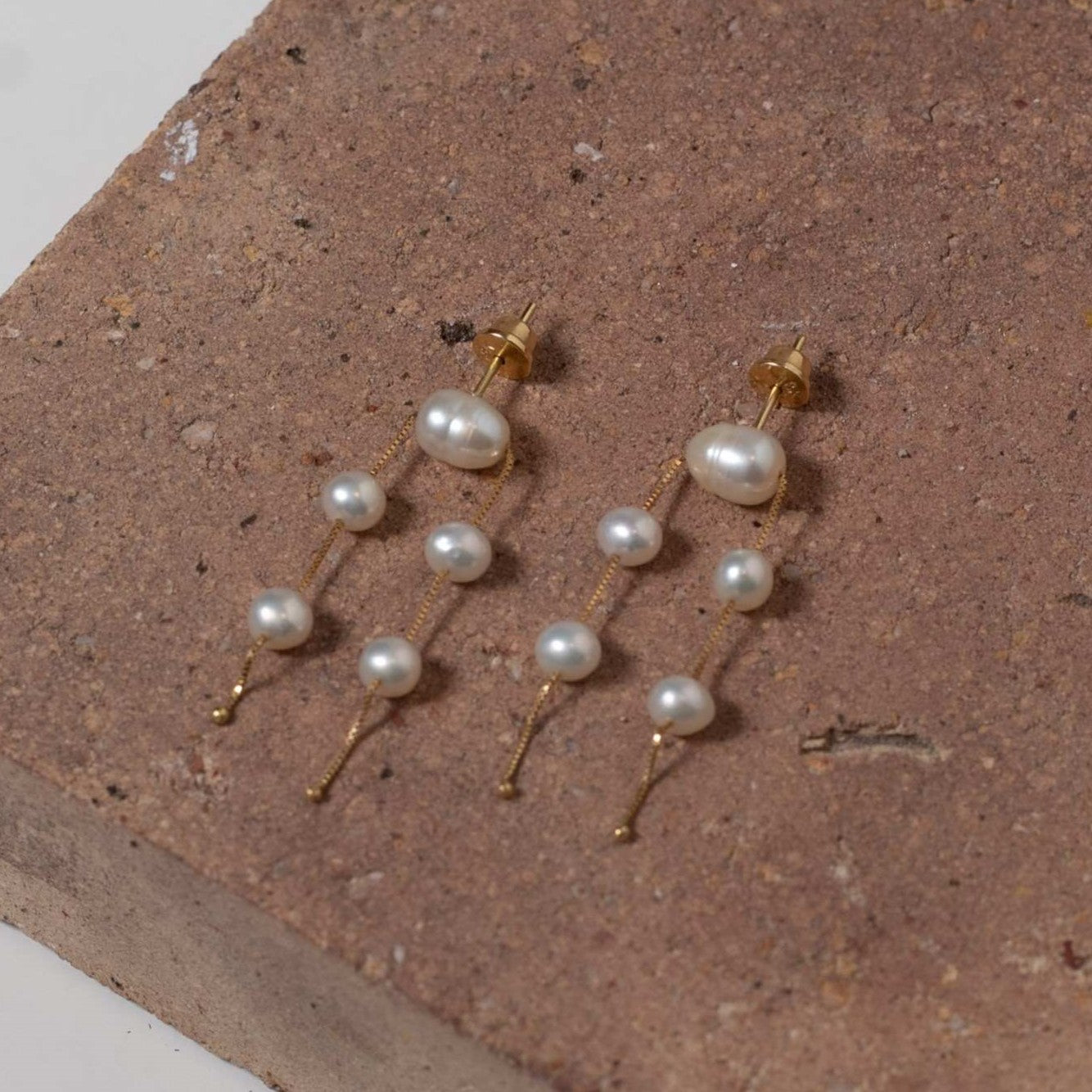 Brinco ouro 18k 5 perolas apoiado em fundo de pedra