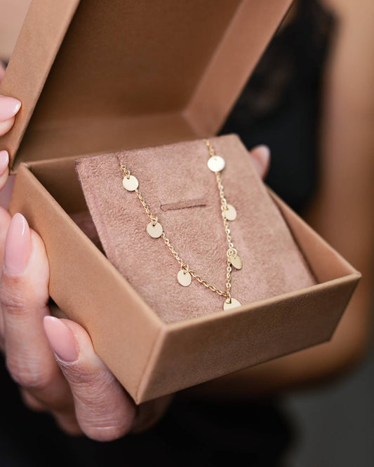 Mulher segurando embalagem com Colar ouro 18k corrente bailarina e medalhas